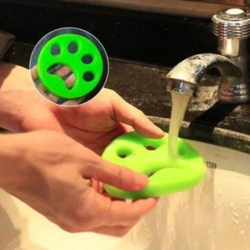 Pet Hair Remover in bright green soft flexible material shaped like a paw, being rinsed under running water by hands